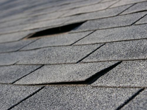 Damaged gray asphalt roof shingles with lifted and missing sections