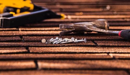 Close-up of roofing tools and nails on wooden shingles, with a red-handled screwdriver