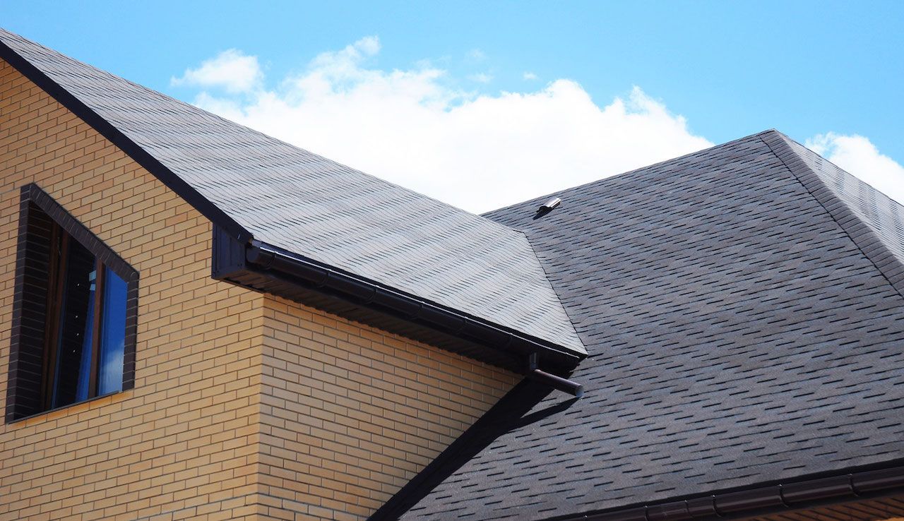 Two-story brick house with dark gray shingled roof against a blue sky