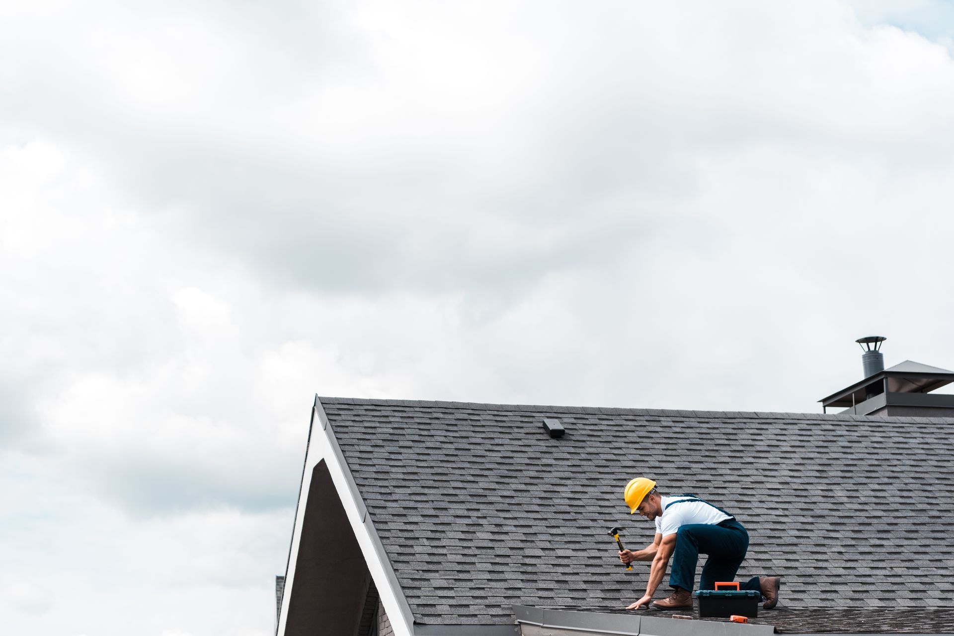 Worker repairing a shingled roof under a cloudy sky
