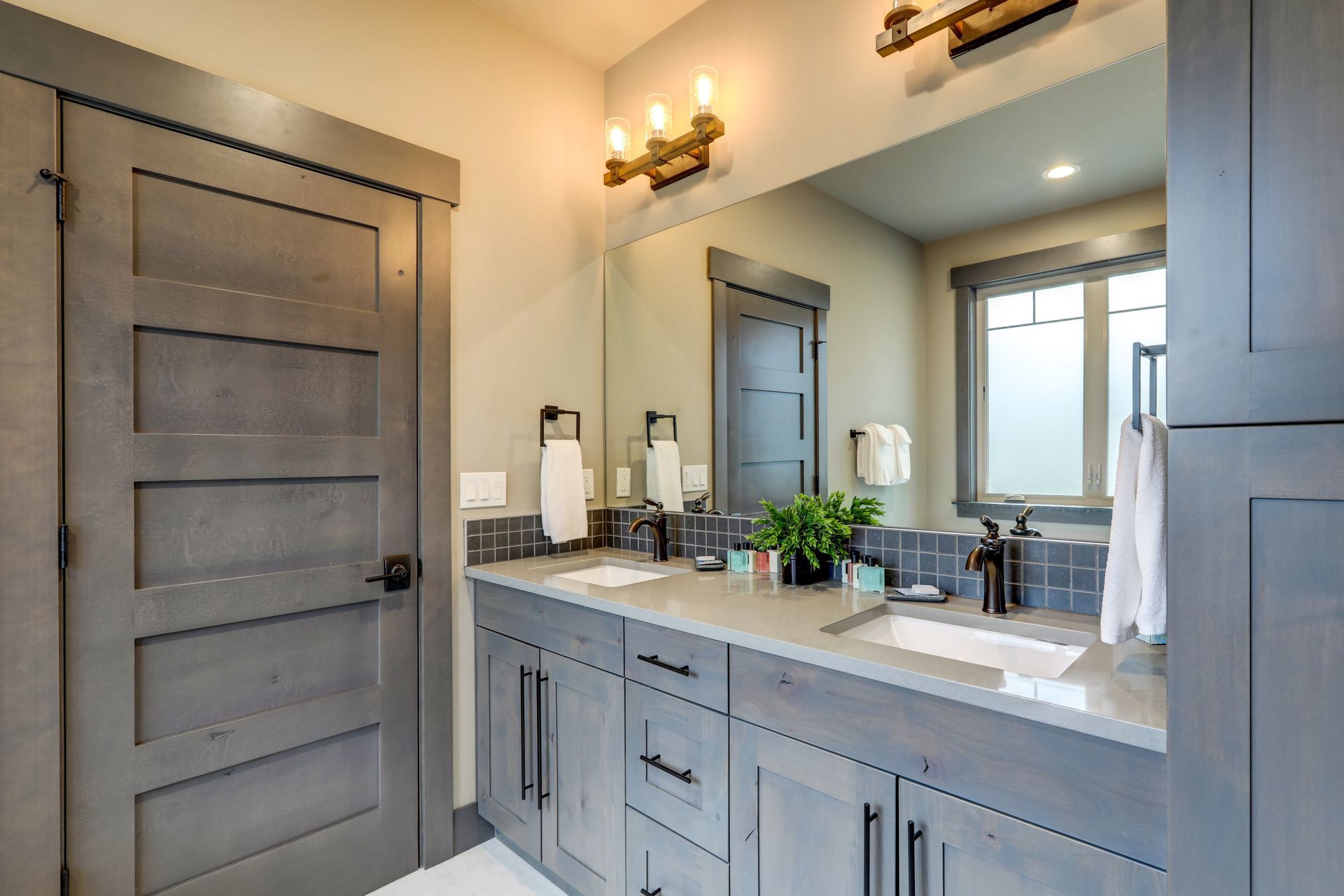 Modern bathroom with gray vanity, large mirror, wall sconces, and a tiled shower door