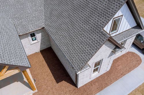 Aerial view of a house roof with white siding, gray shingles, and a brown gravel walkway.