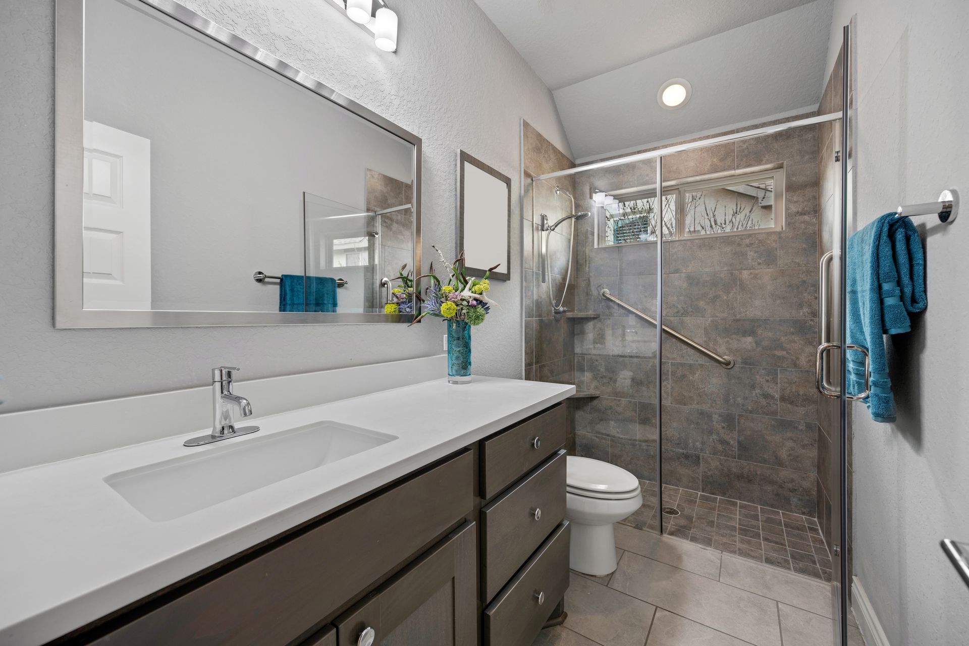 Modern bathroom with vanity, mirror, shower, and toilet in gray and white tones
