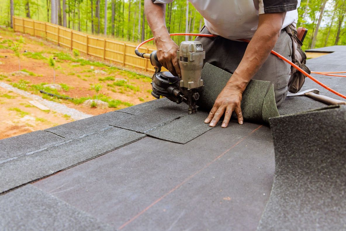 Worker installing black roofing membrane on a sloped roof outdoors
