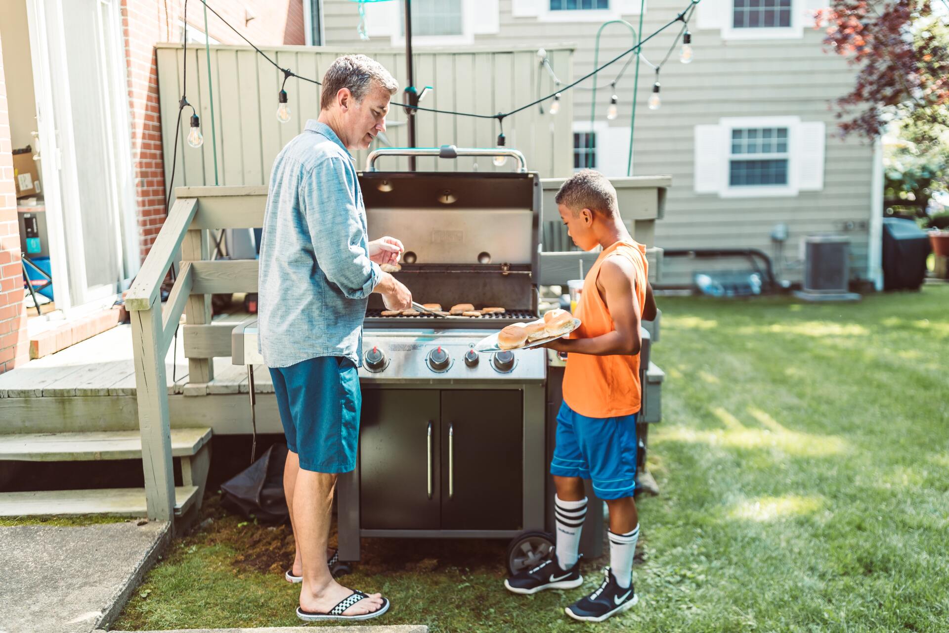 A man and a boy are cooking food on a grill in a backyard.