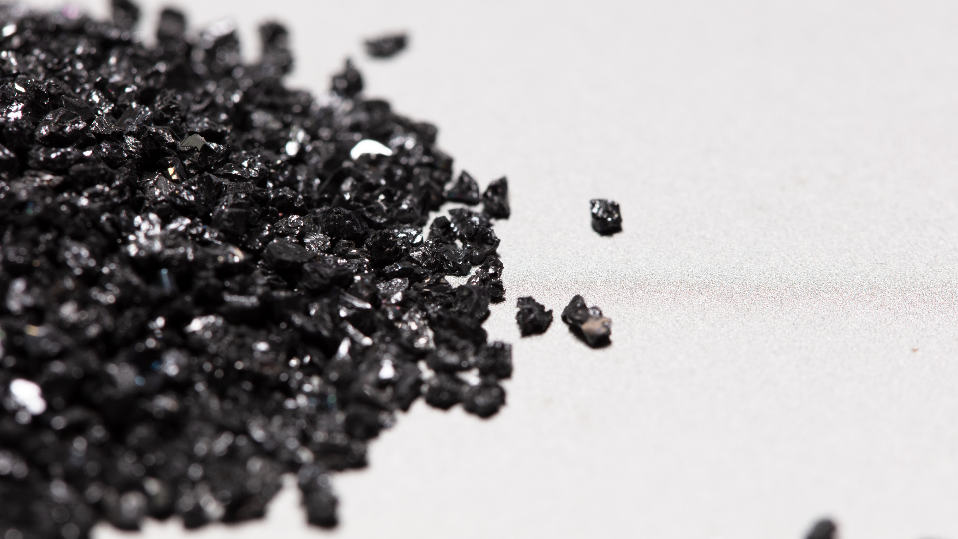 A close-up of a pile of coarse, black granular material on a light-colored, smooth surface.