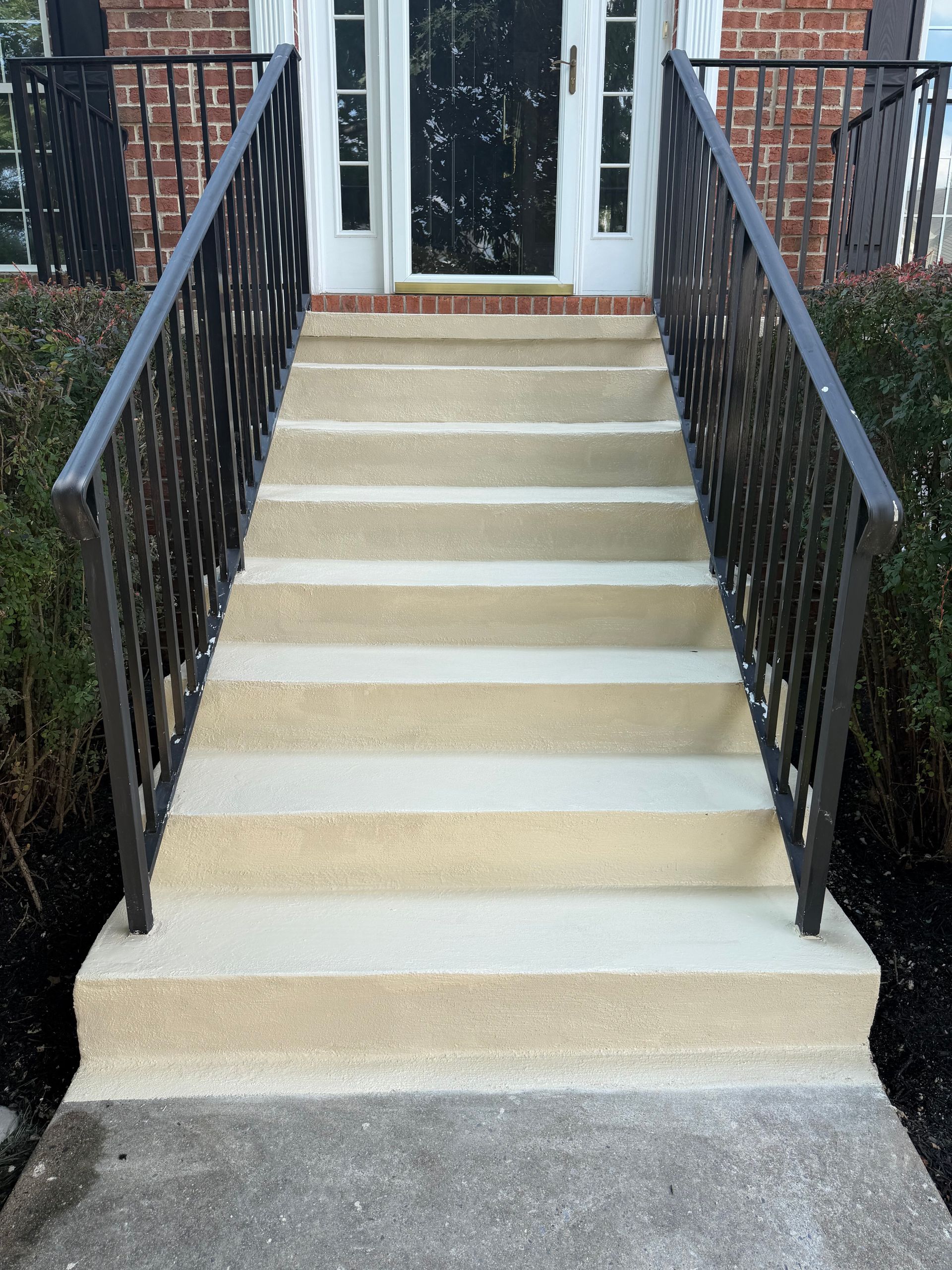 Front steps with black railings leading to a white front door and brick entryway.