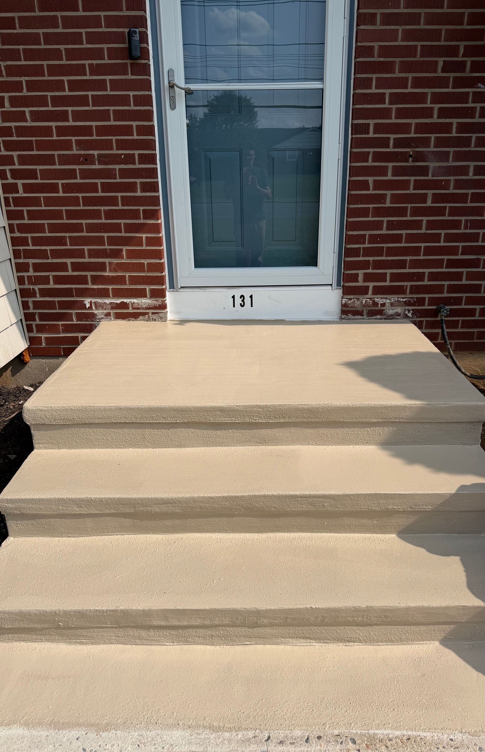Concrete front steps leading to a blue door set in a red brick exterior wall.