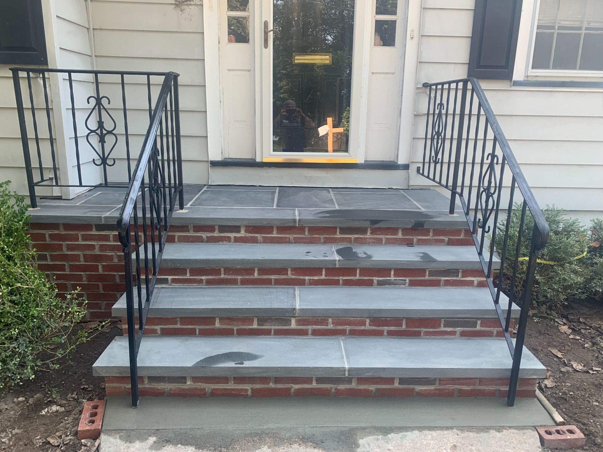 Brick steps with gray stone treads leading to a white door, black iron railings.