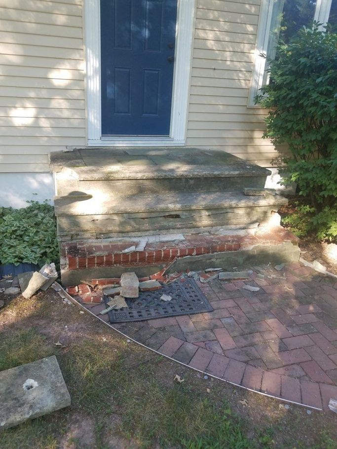 Damaged front porch with crumbling concrete and exposed brick, leading to a blue door.