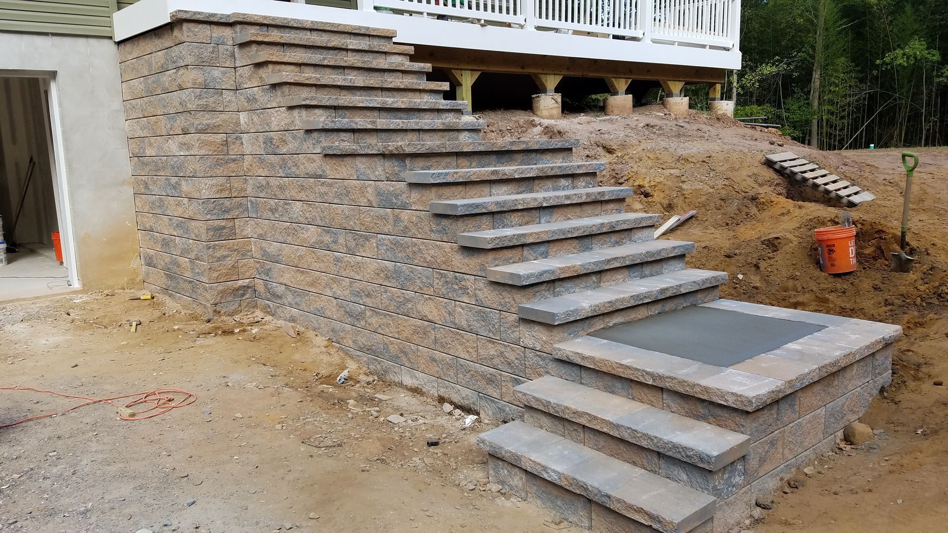 Stone steps and retaining wall leading up to a house with a raised deck. Construction site.