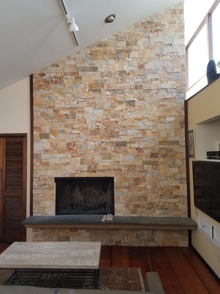 Stone fireplace with dark hearth and surround; light-colored stone wall, slanted ceiling, wooden floor.