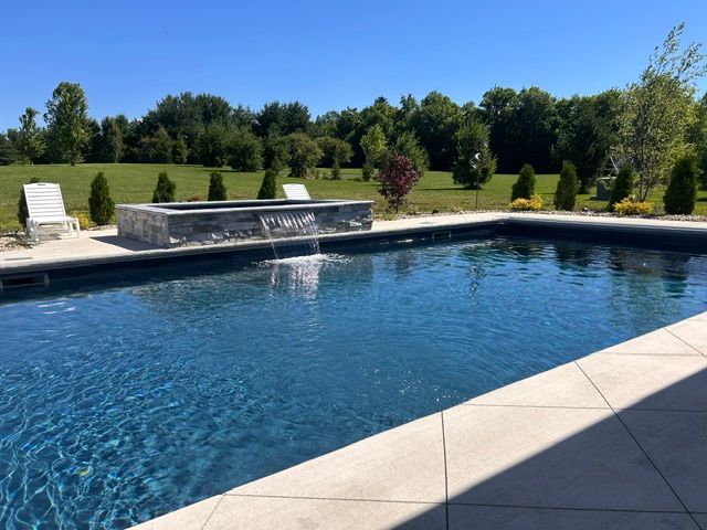 Modern backyard pool with a stone waterfall, lit at night with blue water and landscape lighting