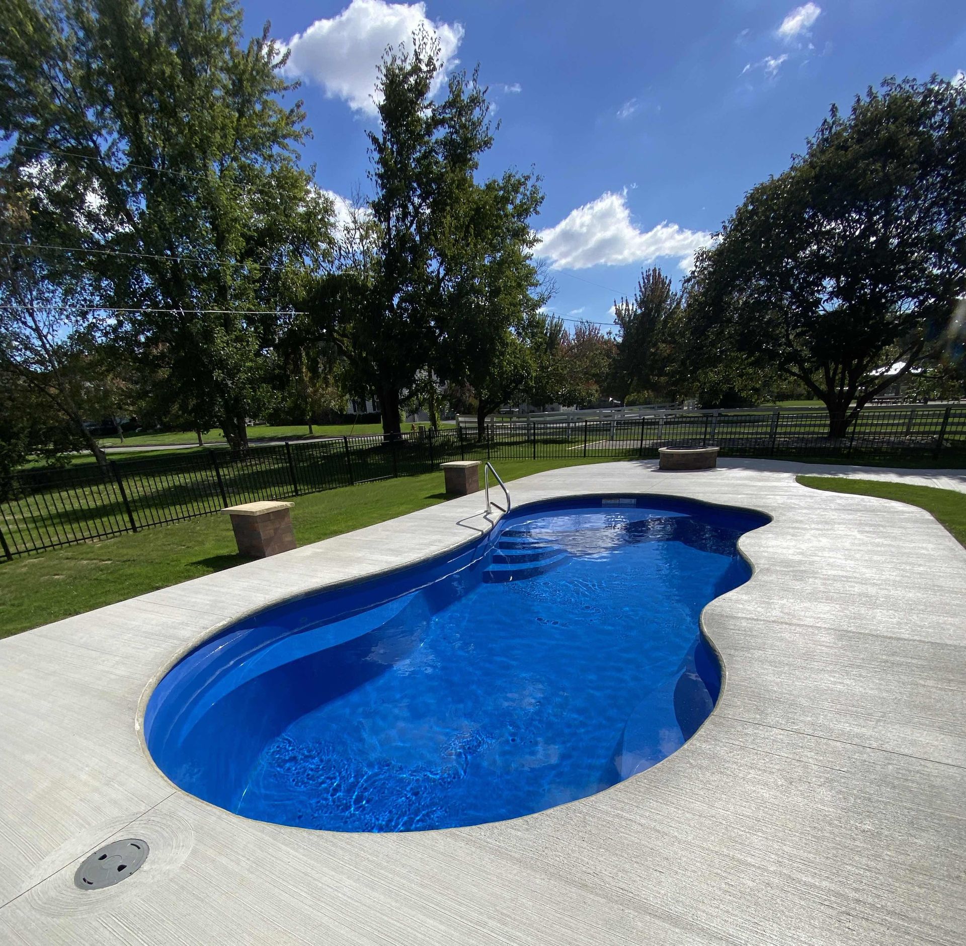 Backyard swimming pool with blue cover beside a house and lawn furniture