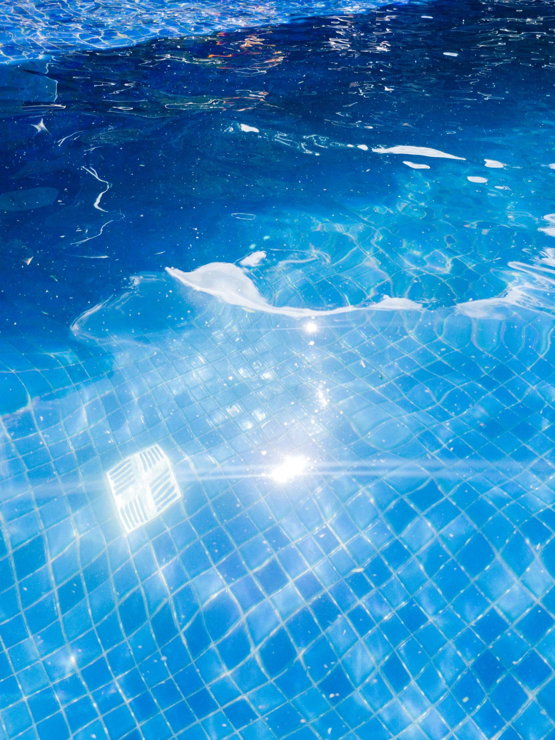 Blue swimming pool water with sunlight reflections and ripples over tiled surface