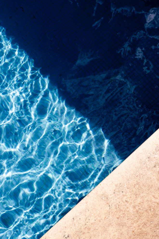 Blue pool water with sunlight ripples beside a beige stone edge