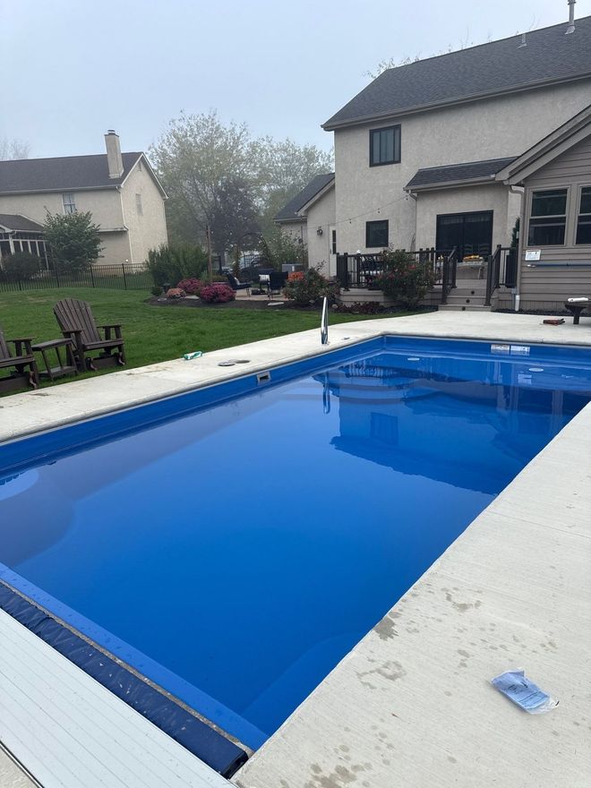 Backyard swimming pool with bright blue water beside a house and patio furniture