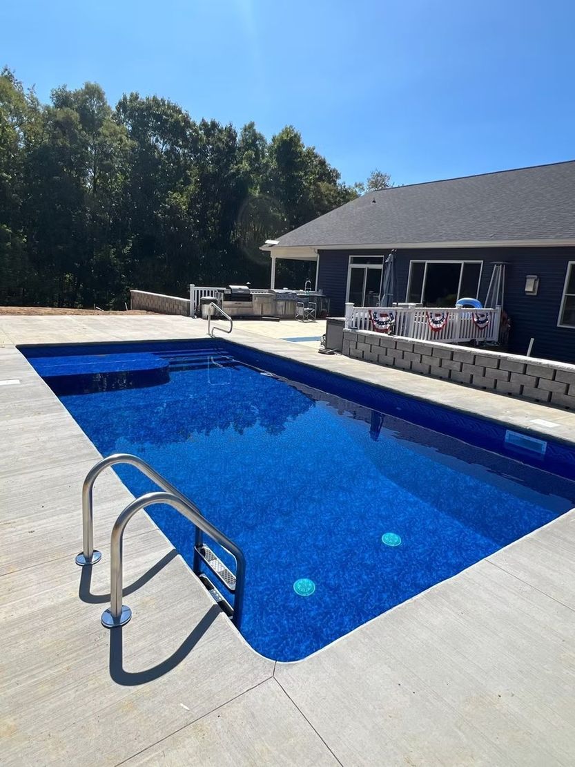 Backyard pool with blue water, concrete deck, ladder, and house patio in bright sun