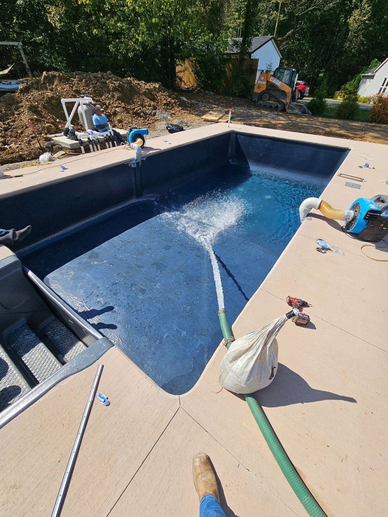 Rectangular in-ground pool being cleaned, with a hose spraying water and tools on the deck