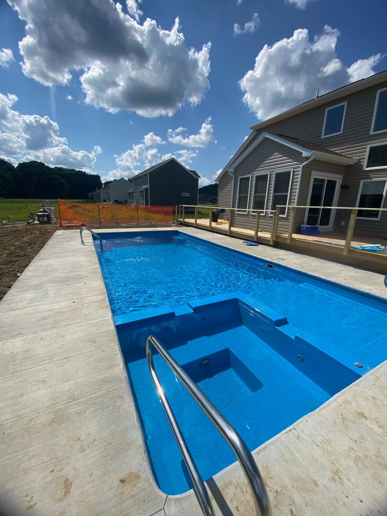 Backyard swimming pool with blue water, steps, concrete deck, and a house under a cloudy sky