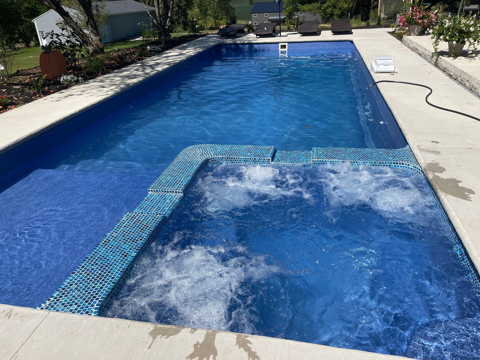 Backyard swimming pool with blue water jets bubbling in the center and a stone deck around it