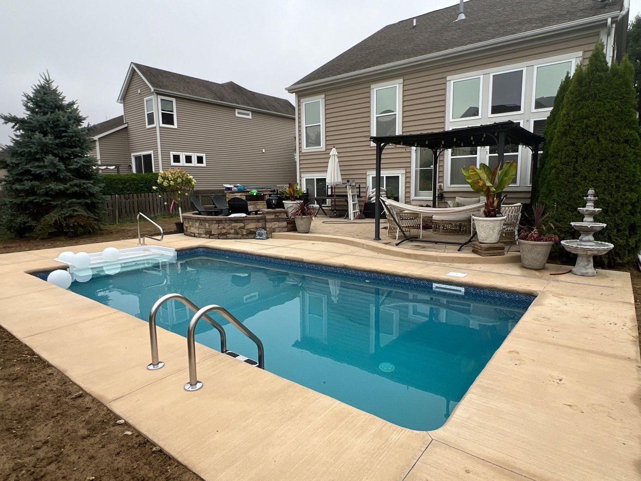 Backyard swimming pool with tan patio, lounge chairs, and houses in the background