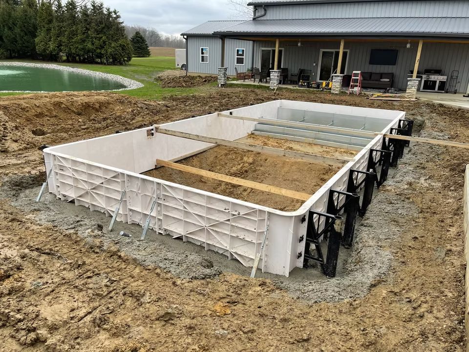 Rectangular concrete foundation formwork at a construction site with dirt and a house in the background