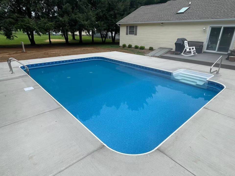 Backyard swimming pool with blue water beside a house and patio chairs