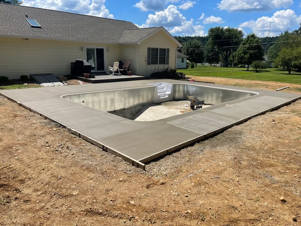 Backyard with a newly built concrete in-ground pool beside a house on a sunny day