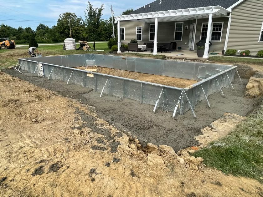 Concrete foundation forms at a house under construction beside a porch and dirt yard.