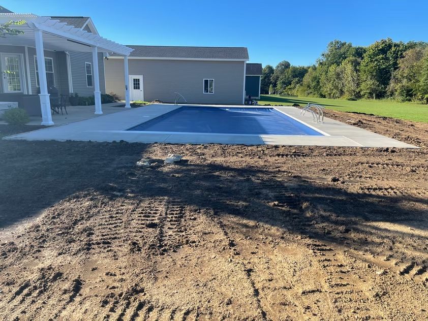 New patio area beside a house with a blue surface, concrete border, and bare ground in front