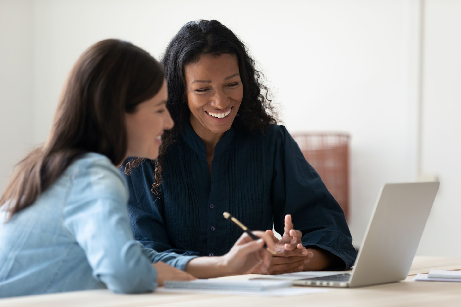 Two women are sitting at a table looking at a laptop computer.