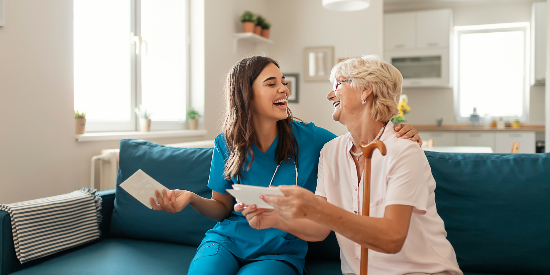 Nurse in blue scrubs smiles at elderly patient in a hospital room.