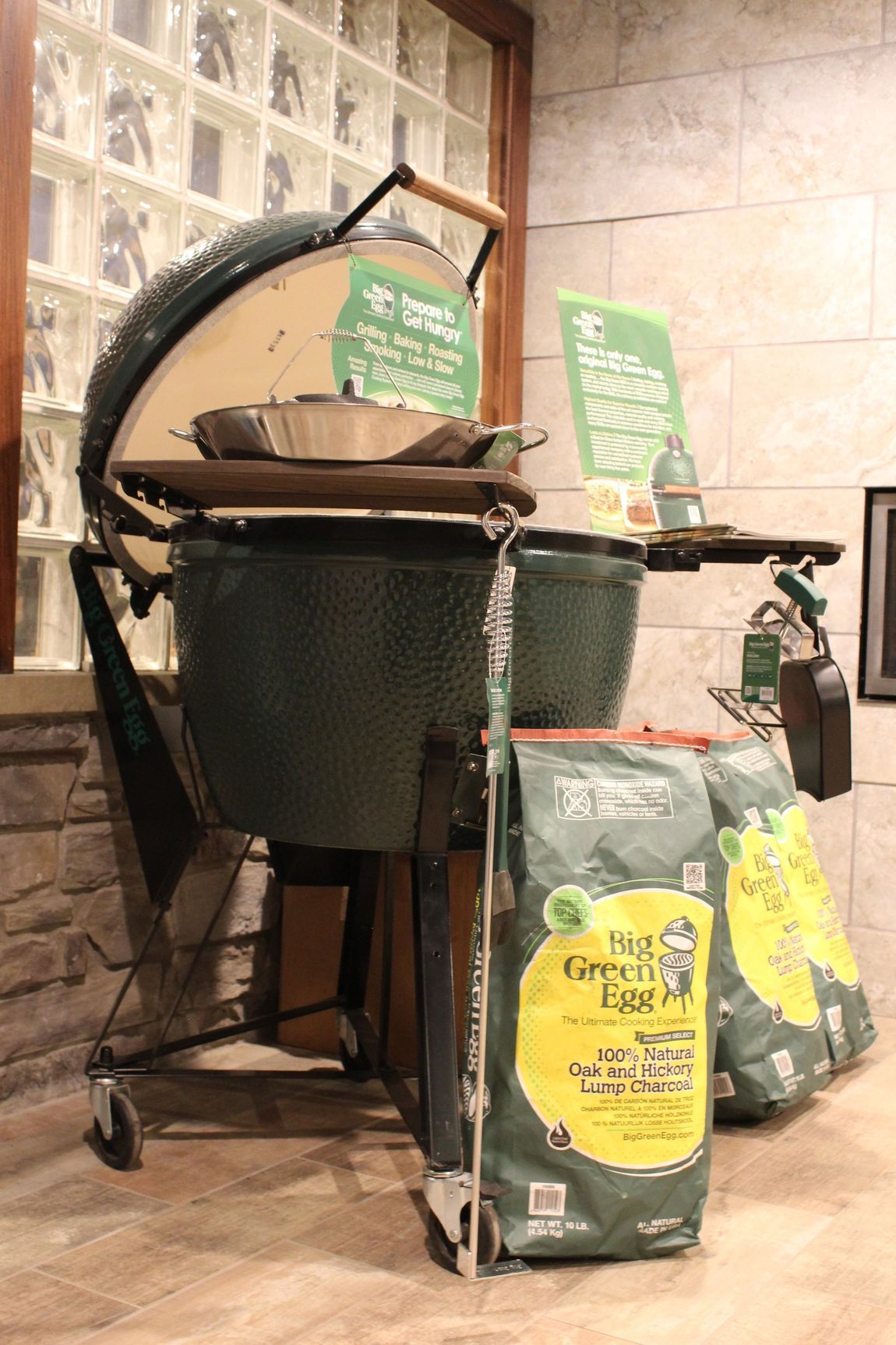 A large green egg grill is sitting next to a bag of big green egg charcoal.