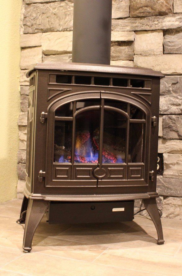 A wood stove is sitting on a wooden floor in front of a stone wall.