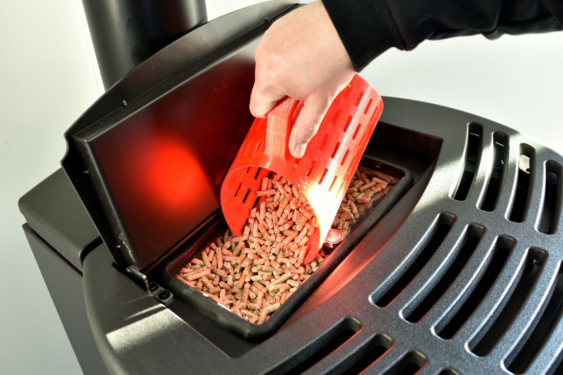 A person is putting wood pellets into a pellet stove