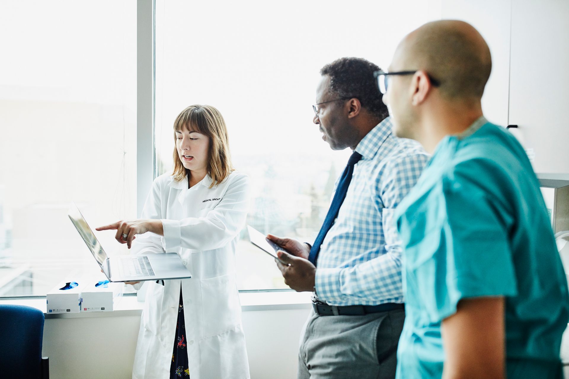A group of doctors and nurses are standing in a hospital room looking at a tablet.