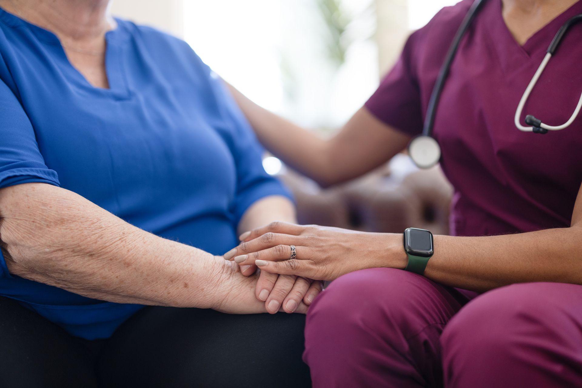 A nurse is holding the hand of an elderly woman.