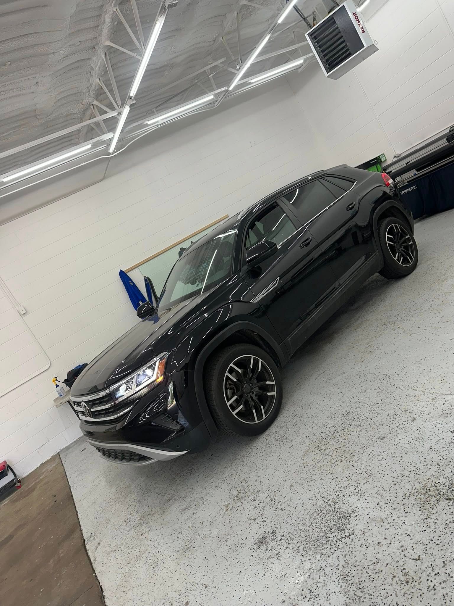 A shiny black SUV parked inside a well-lit garage with a grey speckled floor.
