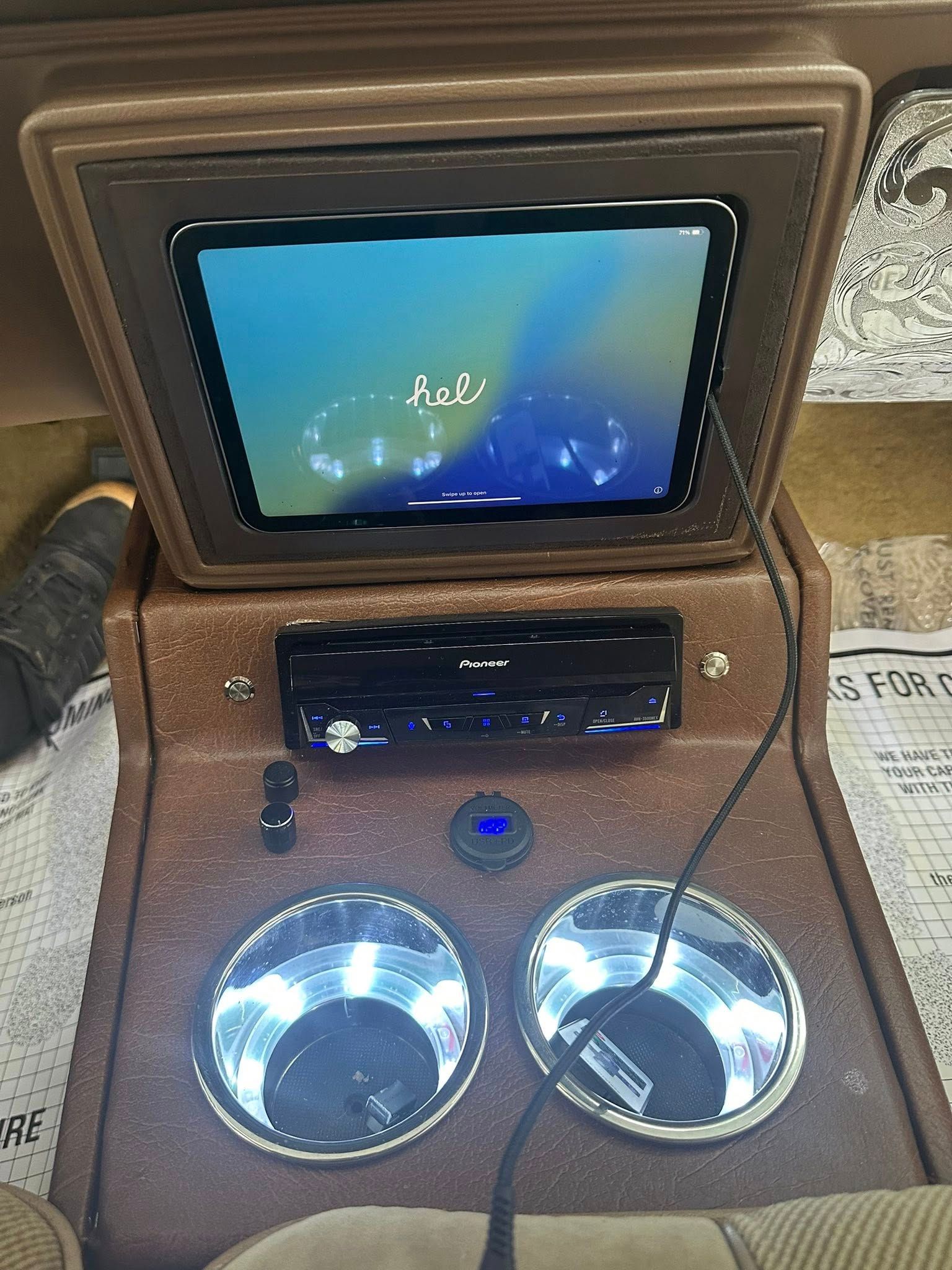A custom brown console featuring a mounted tablet display, a car stereo, two chrome cup holders, and a charging cable.