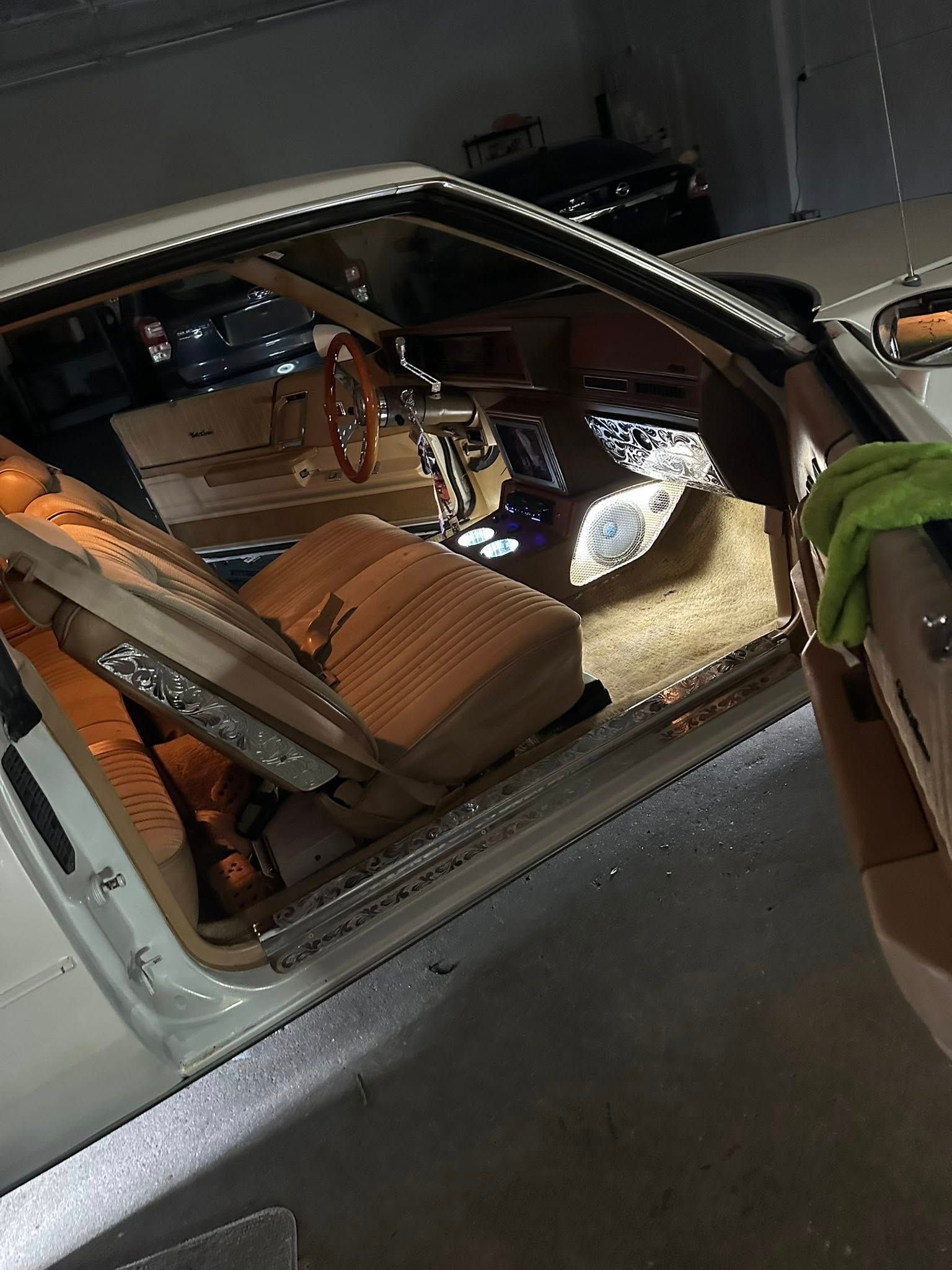 Interior view of a classic car with tan velour bucket seats, a wooden steering wheel, and custom metallic trim.