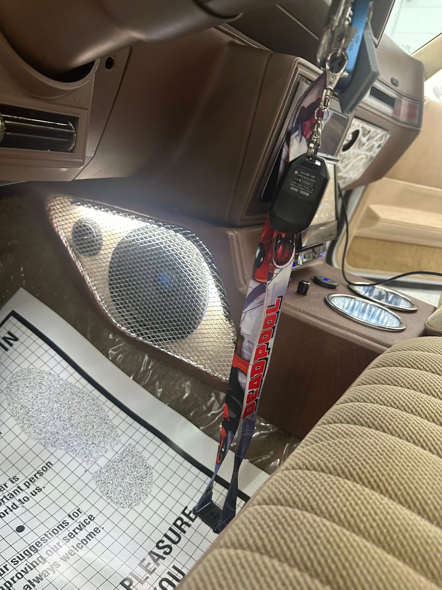 Car interior showing a dashboard with a speaker, tan upholstered seats, and a Deadpool-themed keychain hanging from the dash.