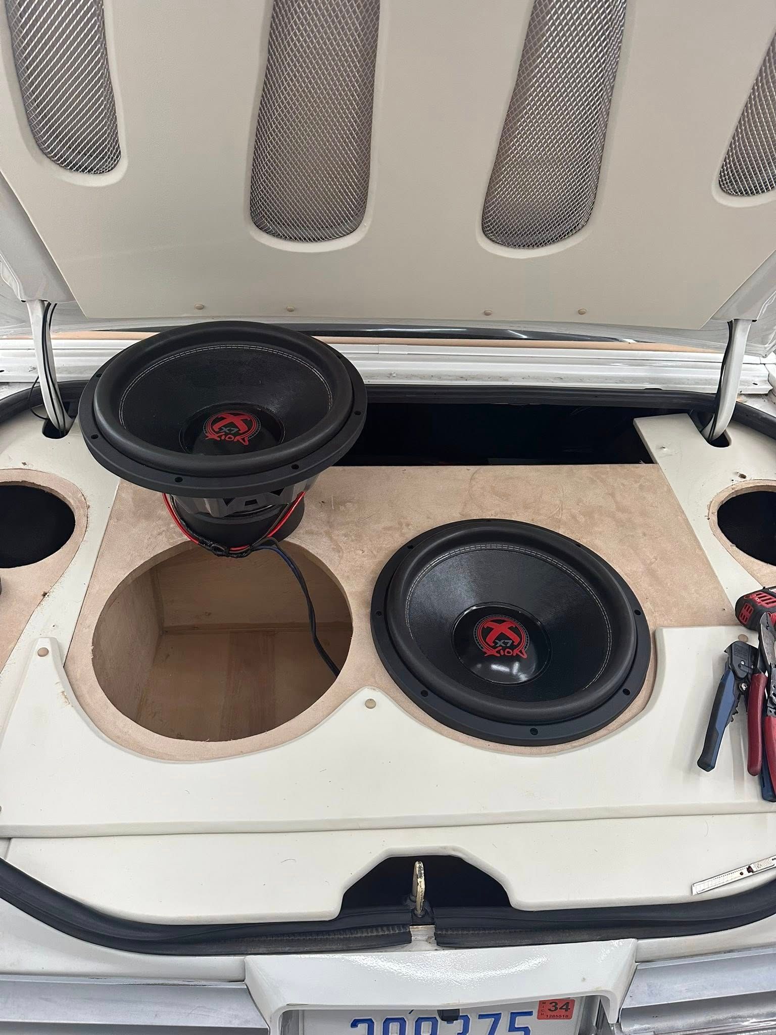 Two car audio subwoofers mounted in a custom trunk enclosure, with one speaker removed, showing internal wiring.