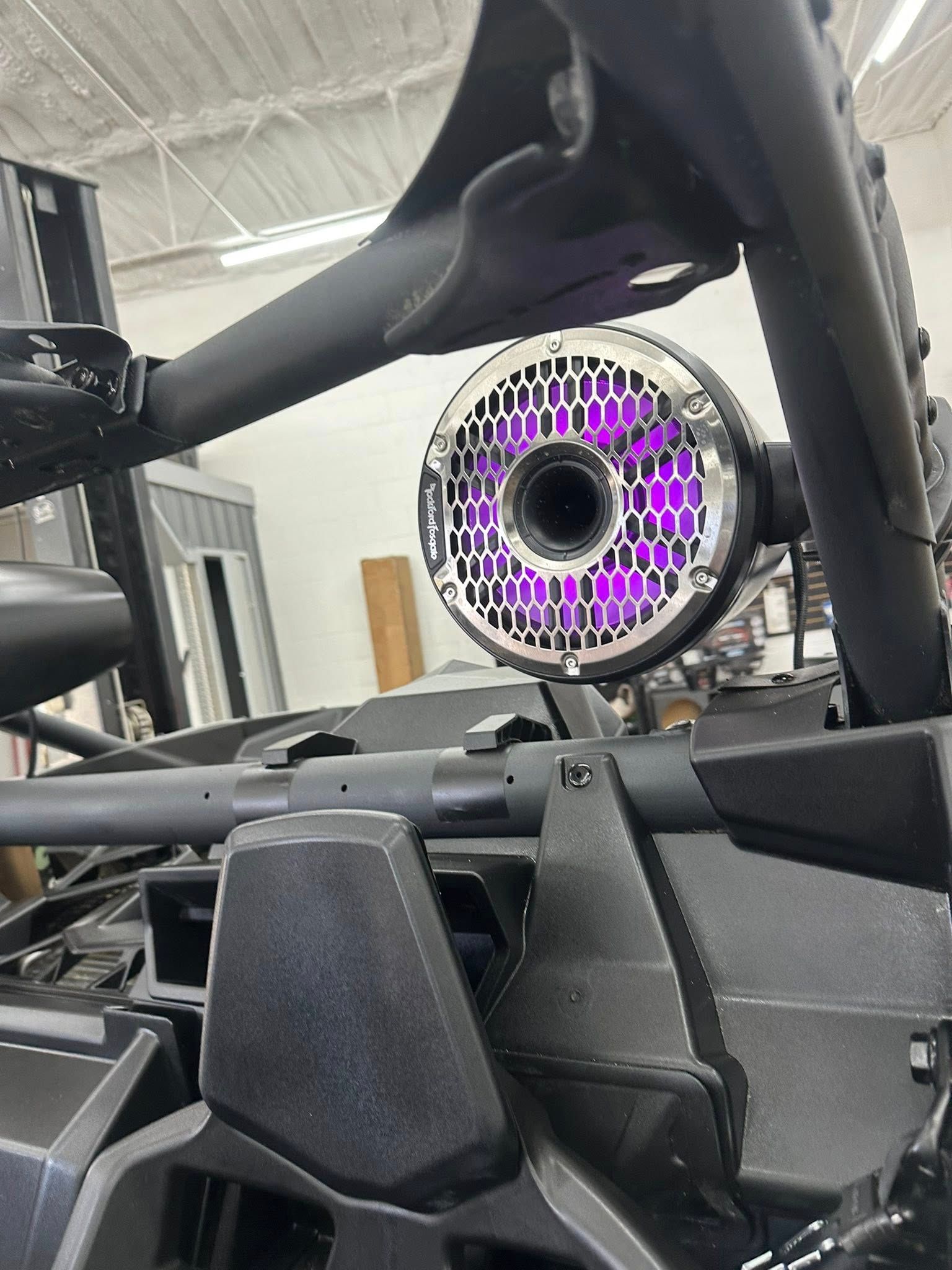 A circular speaker with glowing purple LED lights mounted on the metal roll cage of an off-road vehicle.