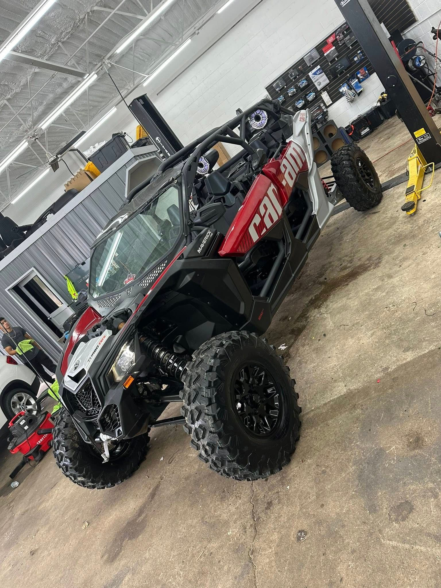 A red and black Can-Am off-road utility vehicle parked on a concrete floor inside a garage.