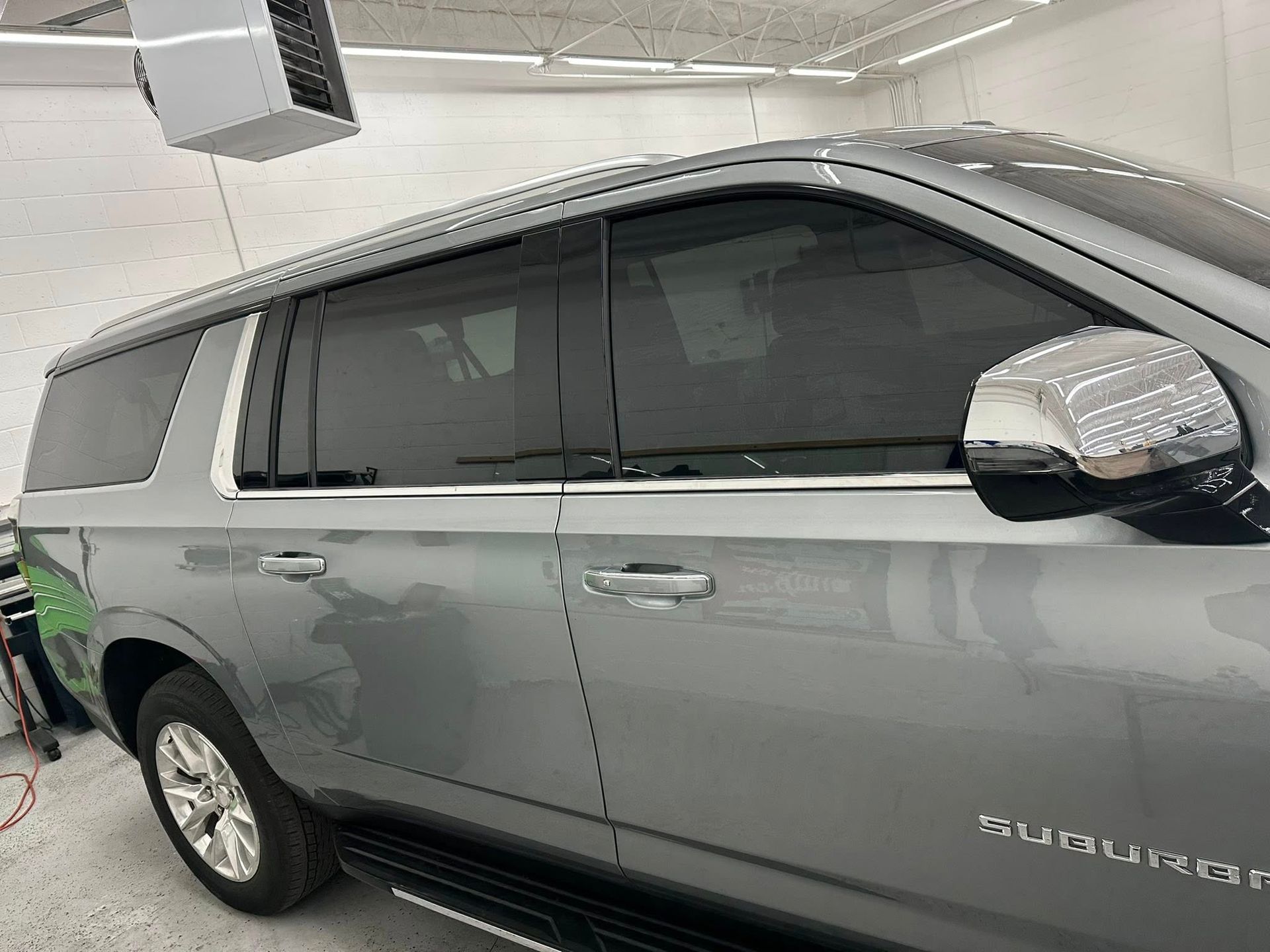 Side profile of a silver Chevrolet Suburban parked inside a brightly lit garage.