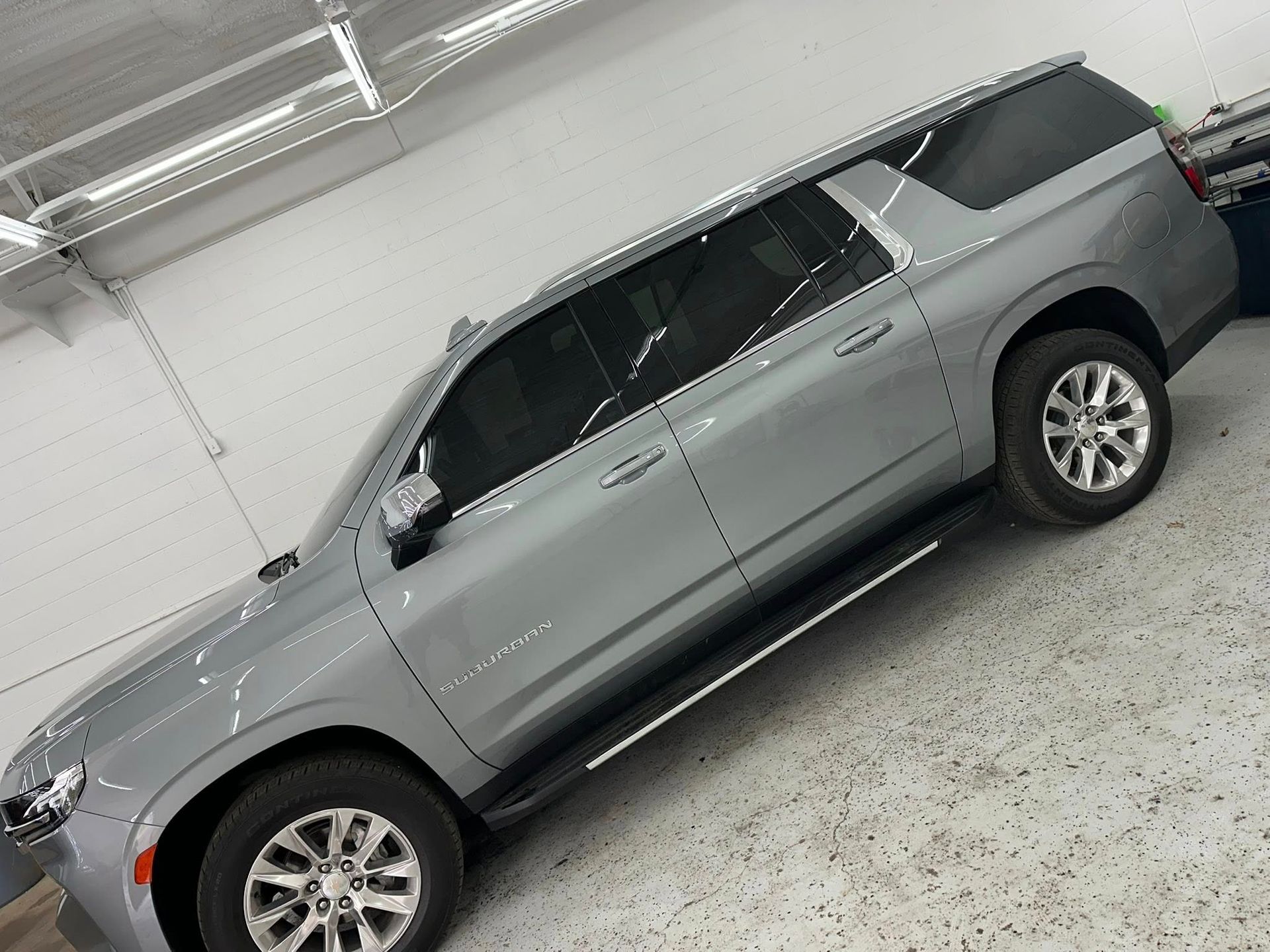A grey Chevrolet Suburban SUV parked at an angle inside a well-lit garage with a white tiled floor.