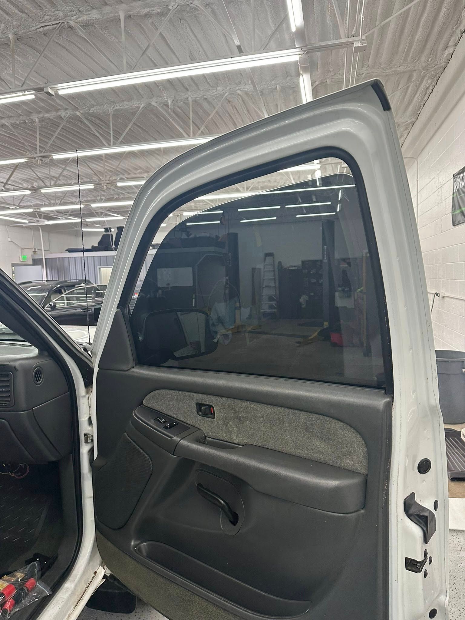 The interior of an open car door with dark tinted windows, dark gray door panel, and fabric trim in a brightly lit shop.
