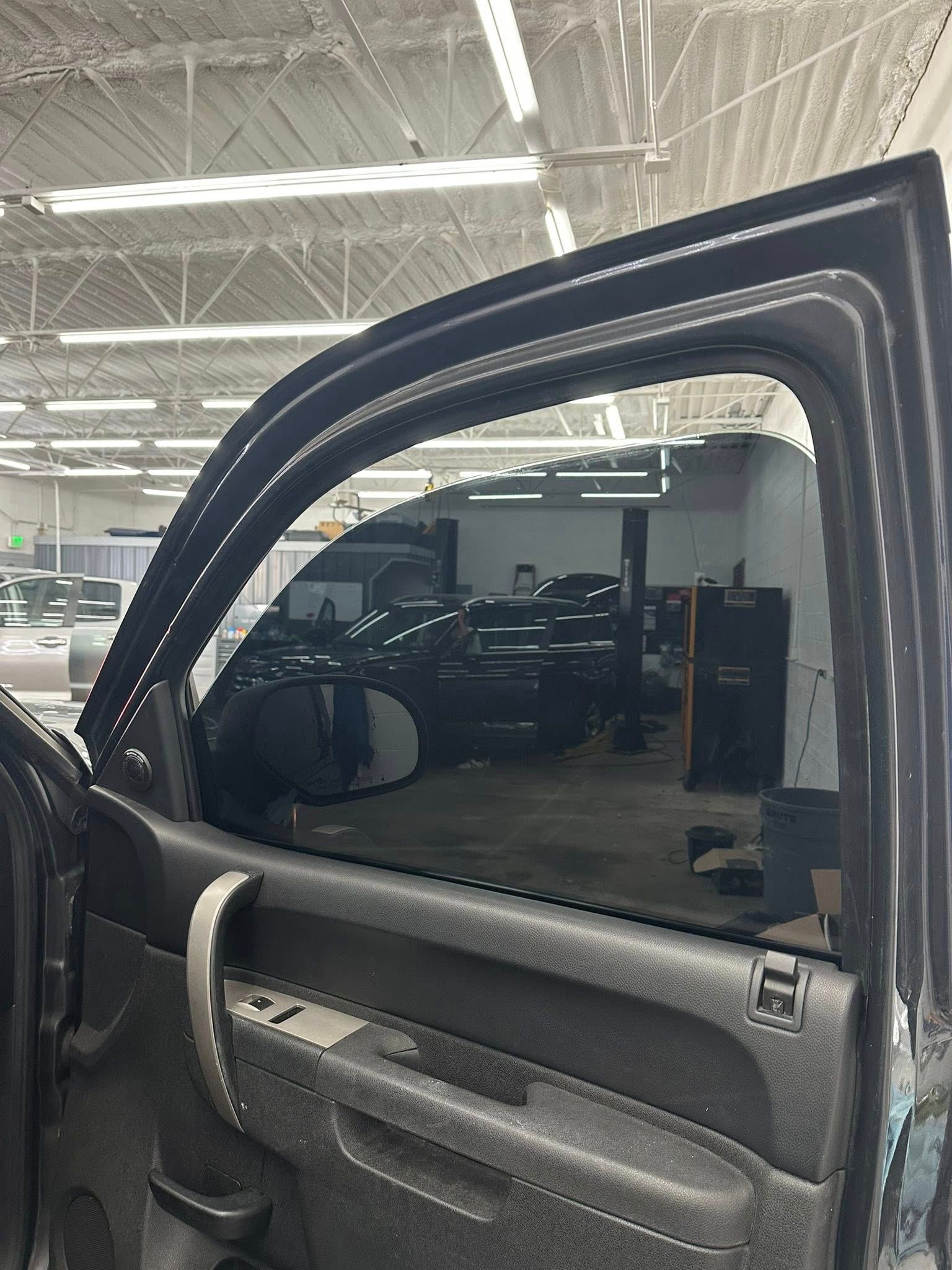 The interior door panel of a dark-colored vehicle showing tinted window glass inside an automotive repair shop.