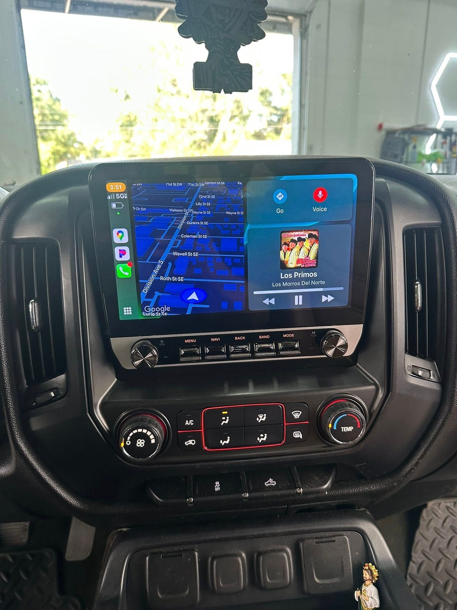 A vehicle's dashboard with a central infotainment screen displaying navigation and media controls above climate buttons.
